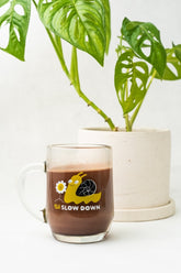 A Blackwing Slow Down Snail Mug with a snail illustration next to a potted plant, serving as a reminder of the slow and steady pace of life.